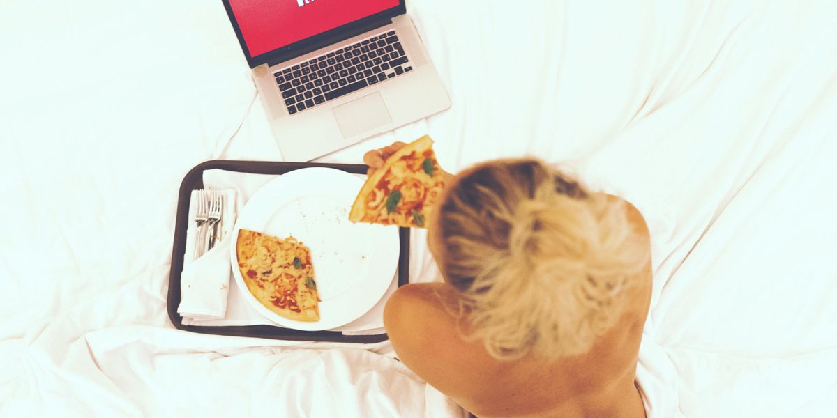 Egy lány az ágyában pizzát eszik Netflix nézés közben