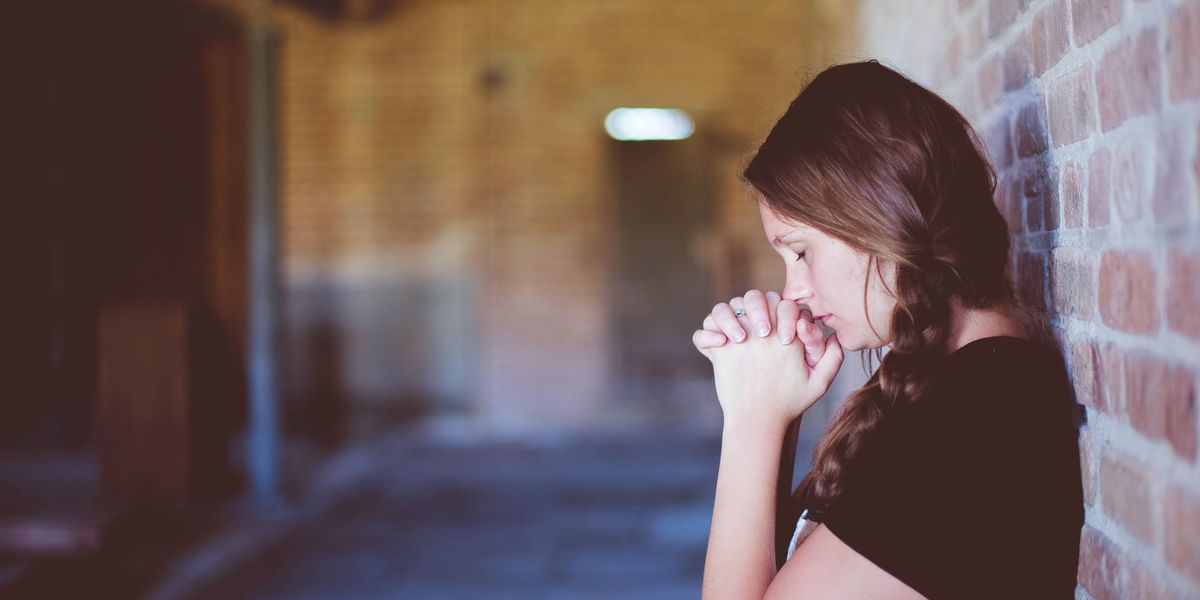 Egy lány falnak dőlve imádkozik
