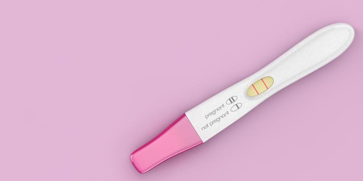 Pozitív terhességi teszt rózsaszín háttéren.