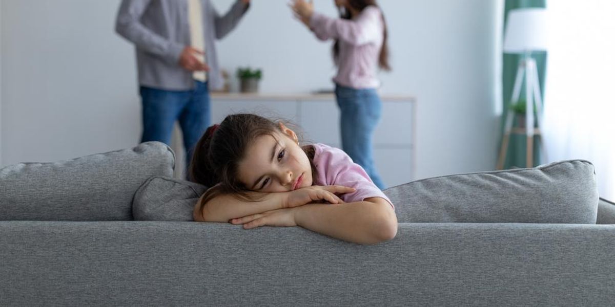 Gyerek egyedül fekszik a kanapén, szülők a háttérben veszekednek