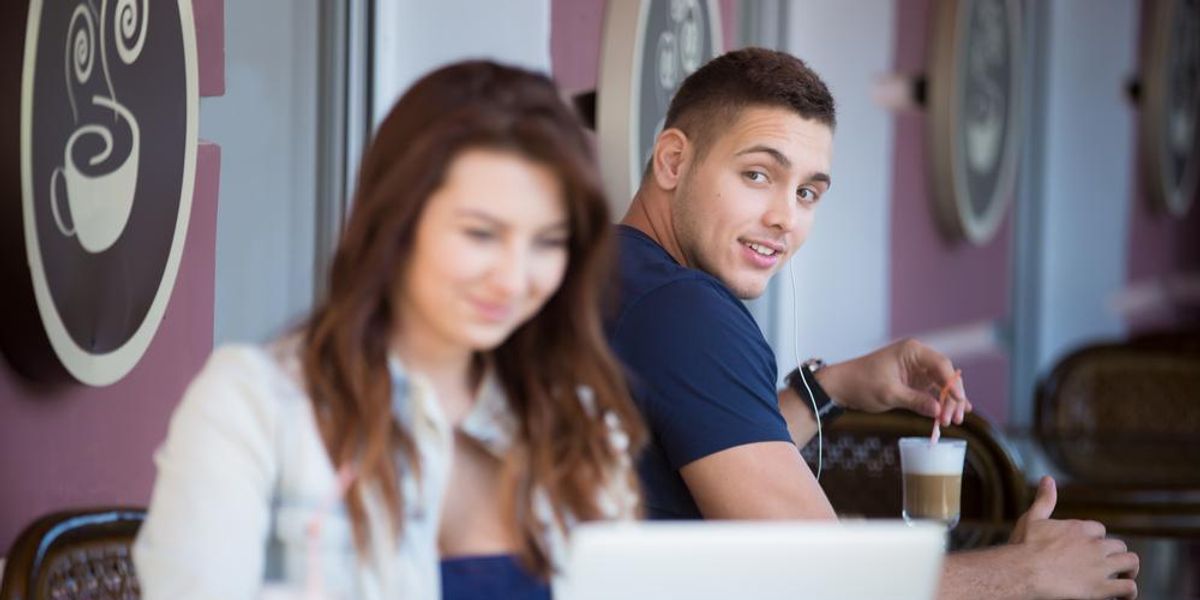 Barna hajú nő laptop előtt ül egy kávézóban, egy férfi nézi