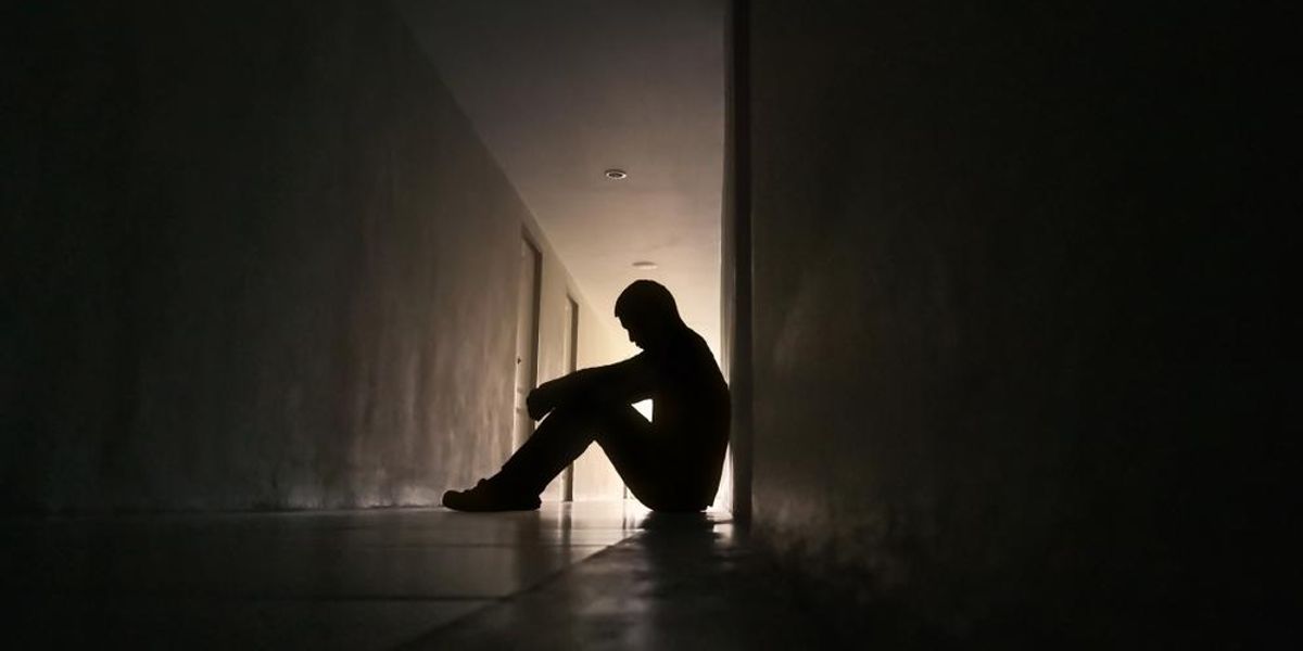 Depressziós férfi sziluettje, aki egy lakóépület folyosóján ül