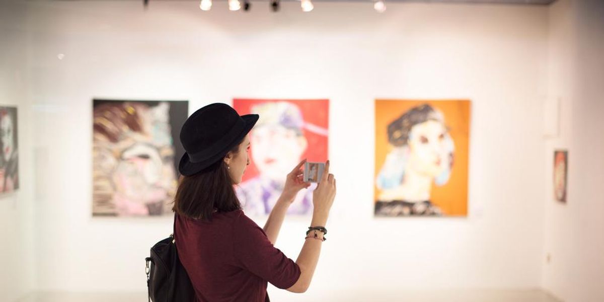 Nő kalapban áll egy művészeti galériában és fényképez