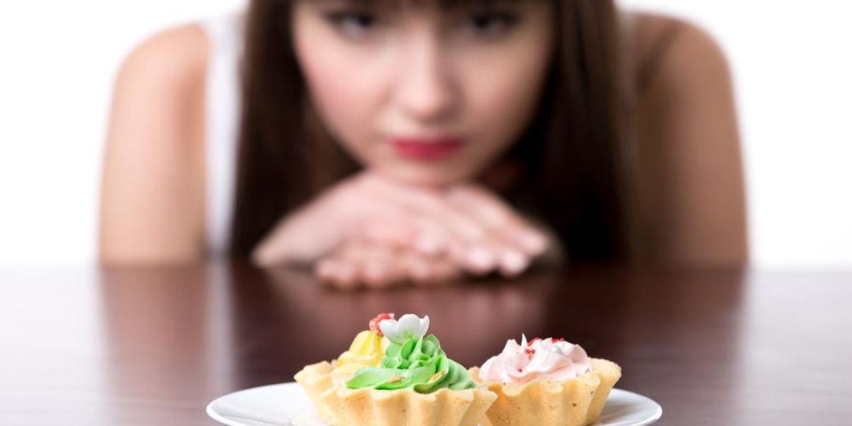 Egy tányér süti előtt ülő nő vágyakozik az édesség után