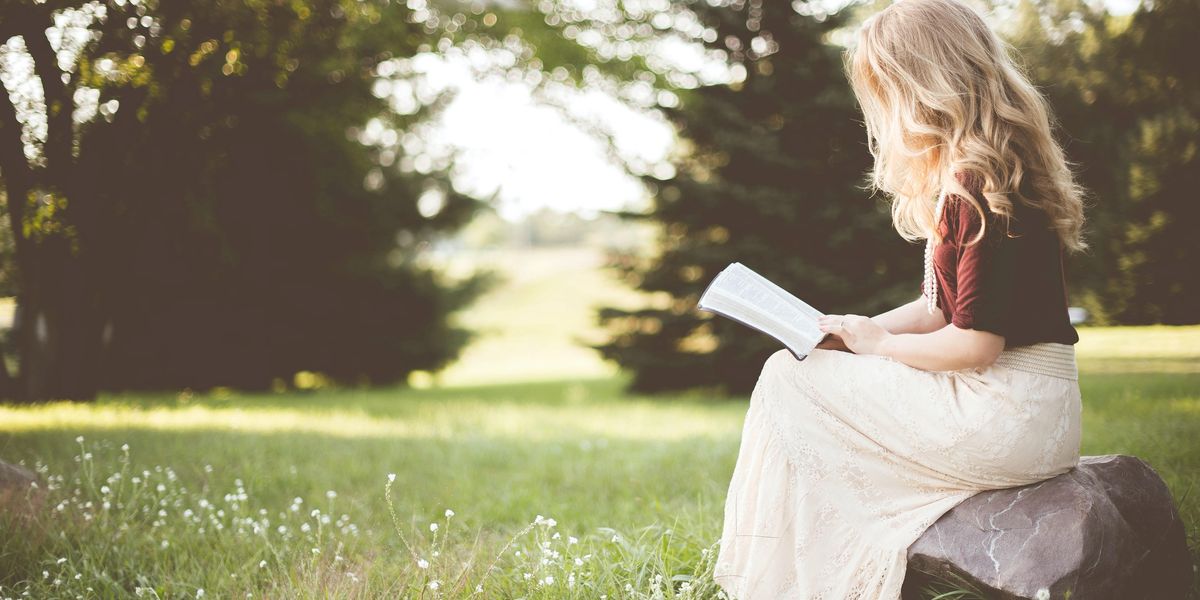 Egy szőke hajú lány könyvet olvas a természetben