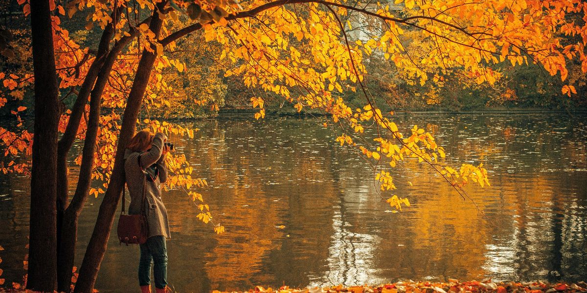 Egy lány egy tó mellett fotózza az őszi tájat