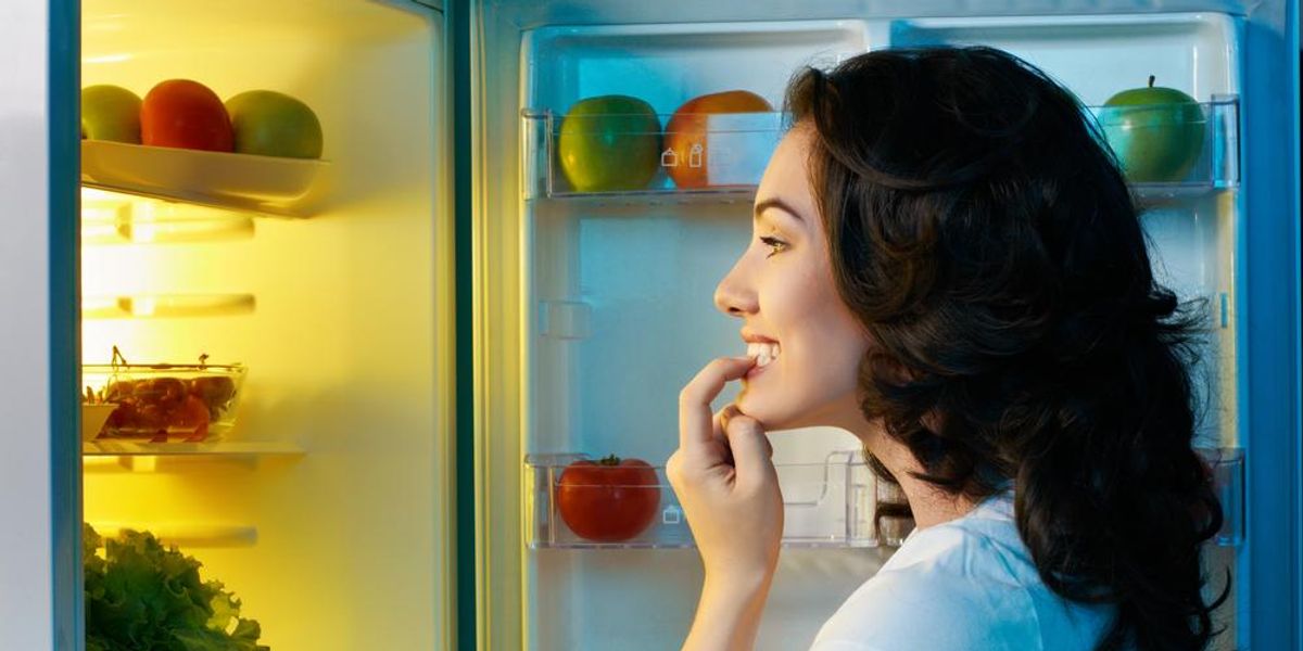 Hűtőben ételt keresgélő nő
