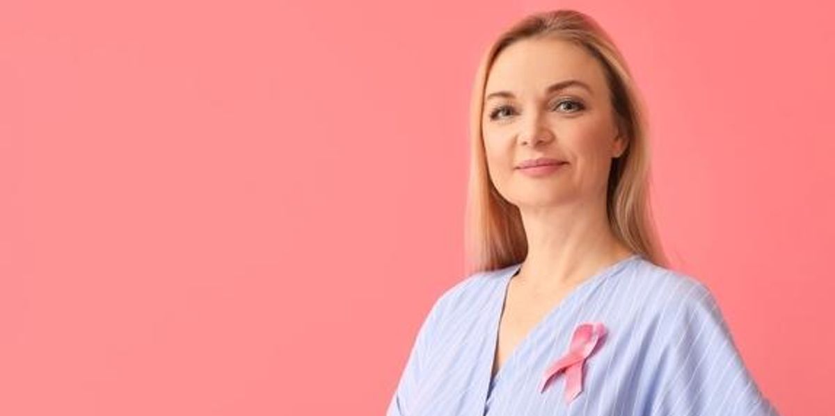 A Mellrák Tudatosság Hónapjának hivatalos szimbólumát, rózsaszín szalagot a pólóján viselő nő, rózsaszínű háttér előtt