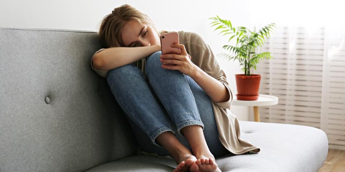Depressziós nő a kanapén ülve mobilozik
