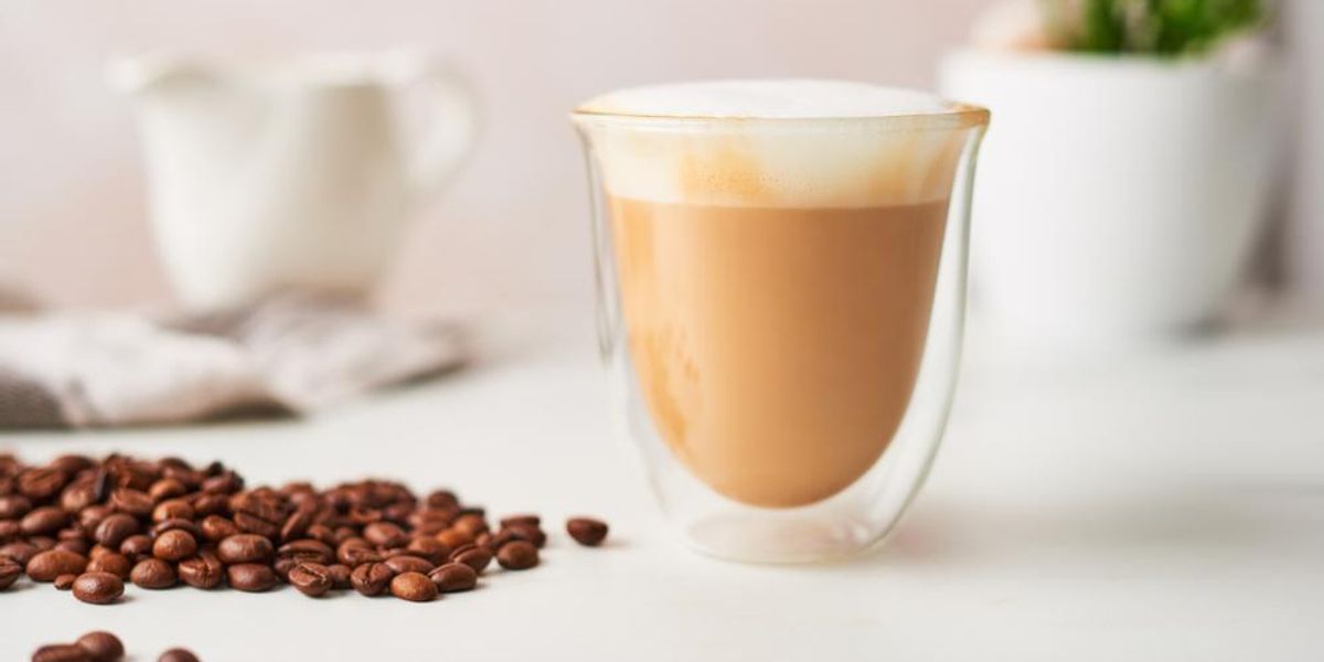 Cappuccino pohárban, pörkölt kávébabokkal az asztalon