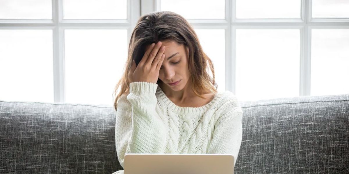 Nő aggódva a homlokát fogja a laptopja előtt ülve a kanapén