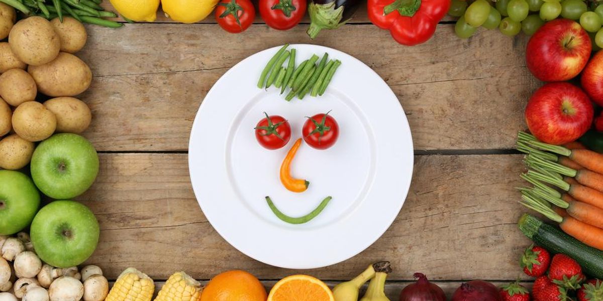 Mosolygó arc a tányéron lévő zöldségekből és gyümölcsökből