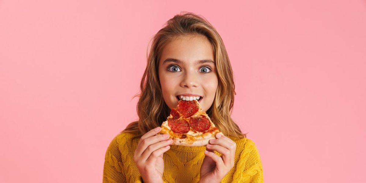 Sárga pulcsiban szőke nő szalámis pizzát eszik