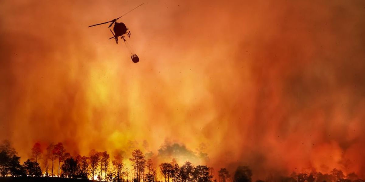 Erdőtűz, az égen helikopter vizet szállít az eloltáshoz