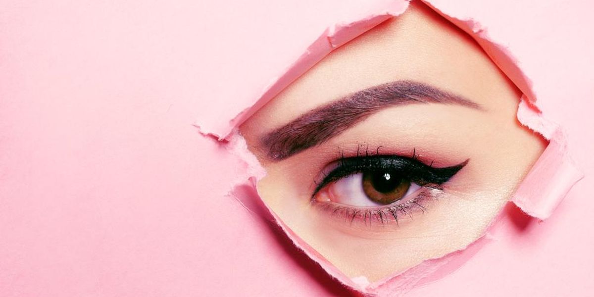 Rózsaszín papír lyukon néző női szem