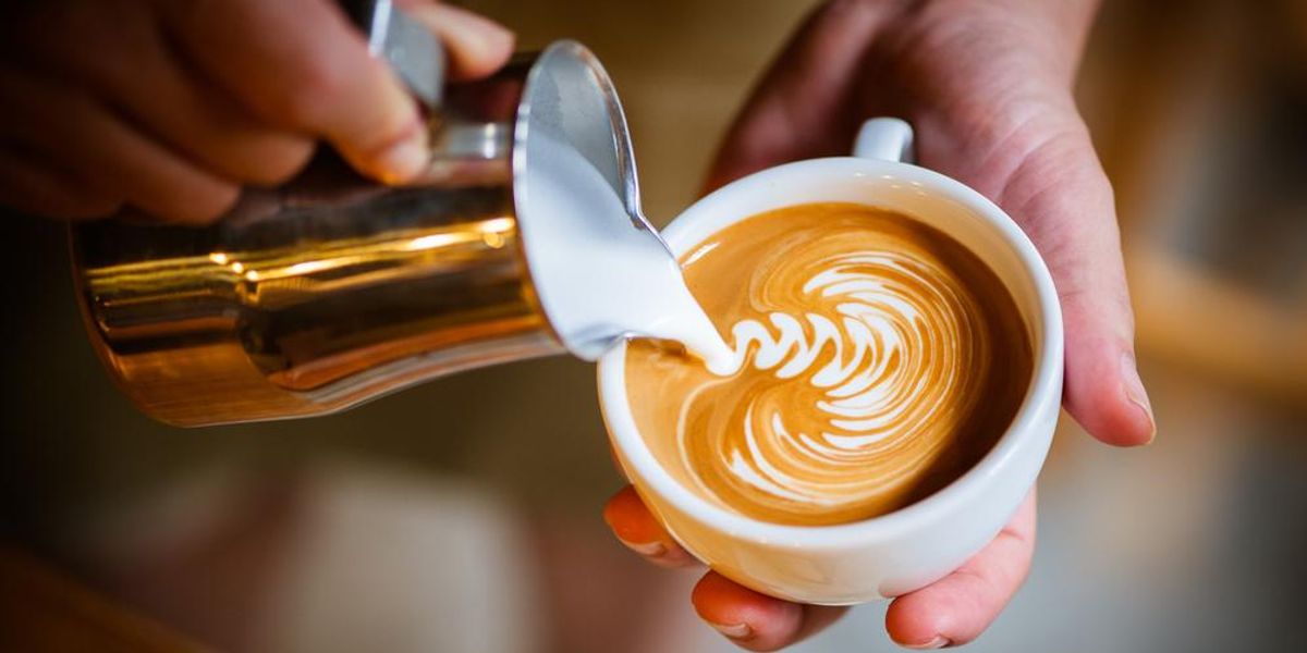 Kávéscsészébe latte artot készítő kéz