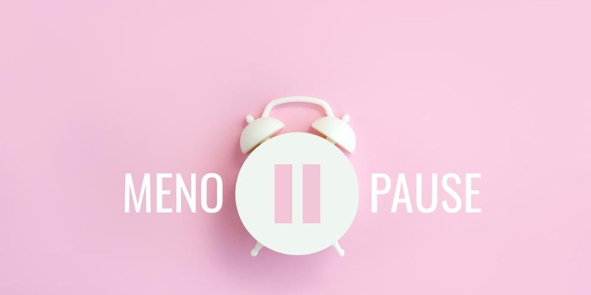 Menopauza szó fehér ébresztőórával, rózsaszín háttéren