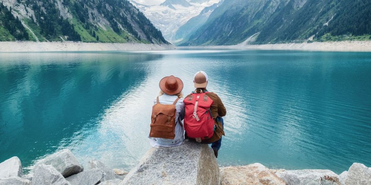 Hegyek övezte tó előtt ülő turista pár