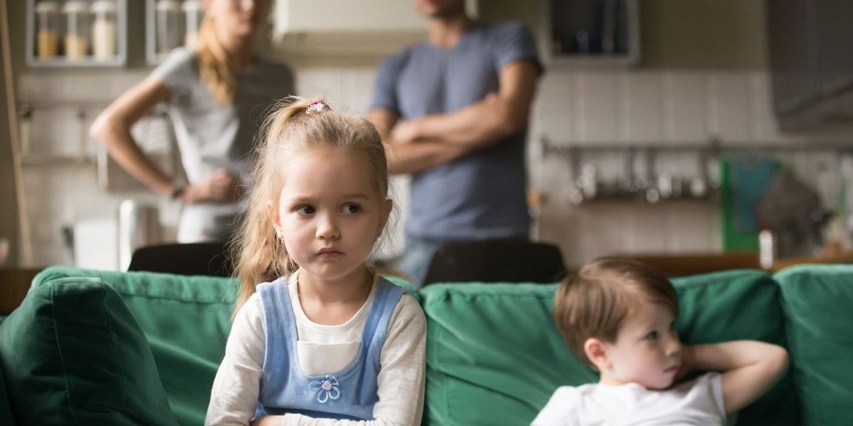 Szülők a háttérben állnak, gyerekek a kanapén ülnek