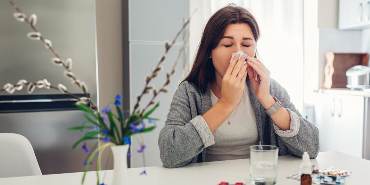 Allergiás nő ül az asztalnál gyógyszerek előtt és fújja az orrát