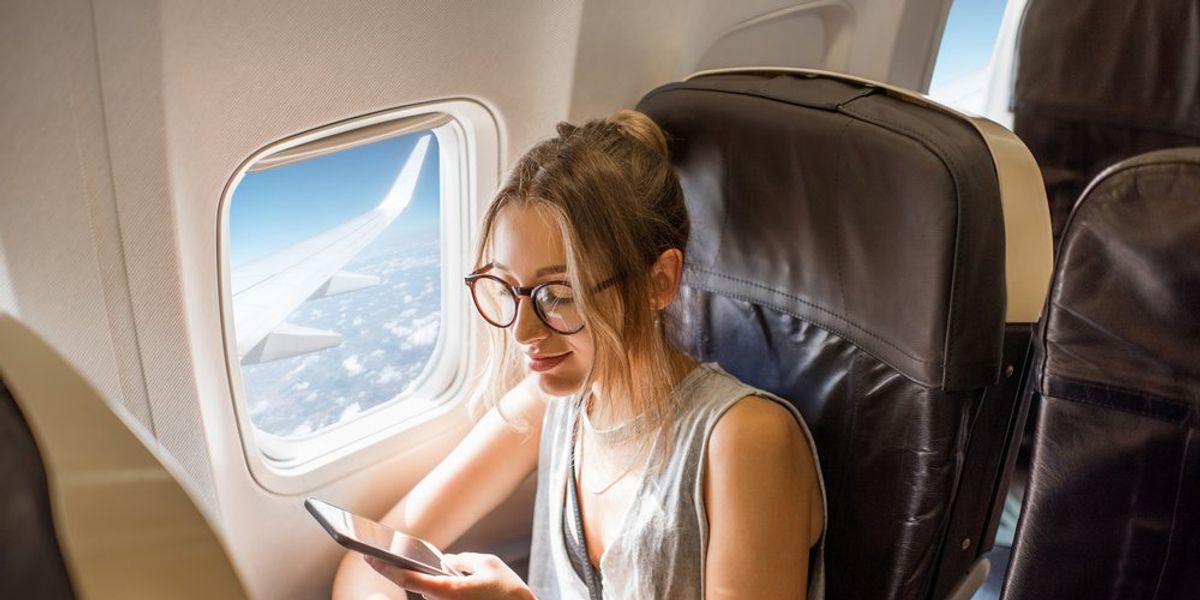 Nő ül a repülőgépen az ablak mellett és a telefonját nézi