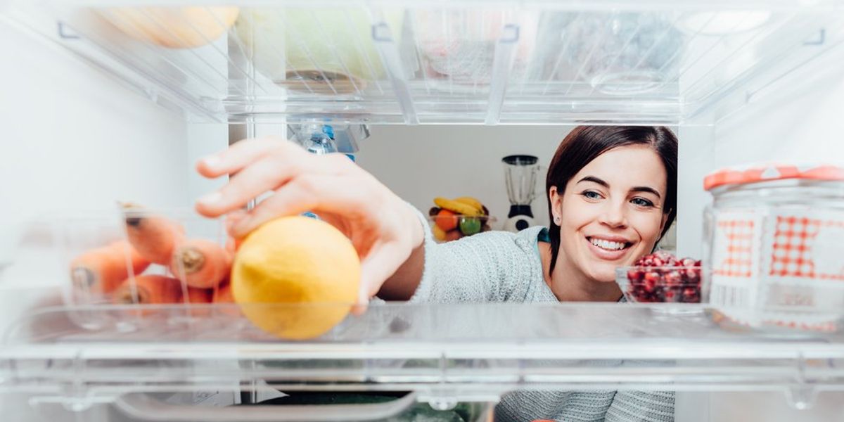 egy mosolygó nő a hűtőbe nyúl egy citromért