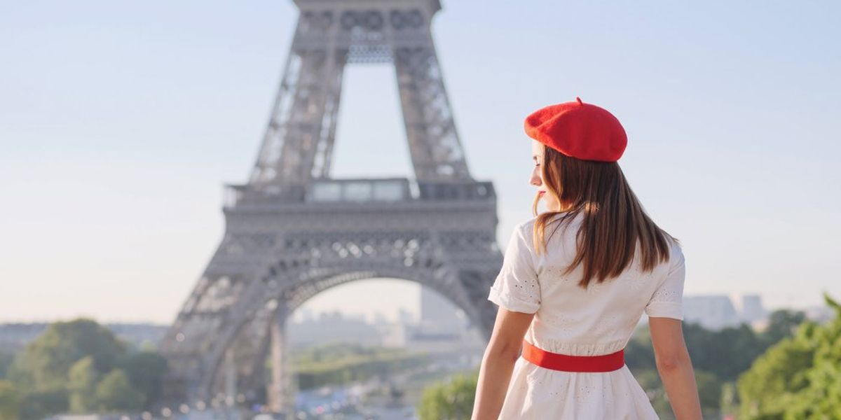 Párizsi lány az Eiffel-torony előtt ül piros sapkában és fehér ruhában