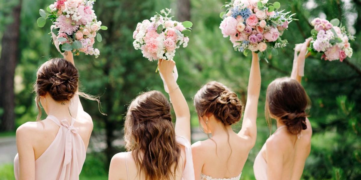 4 nő áll háttal a kamerának, virágcsokrokat emelnek az égbe esküvőn