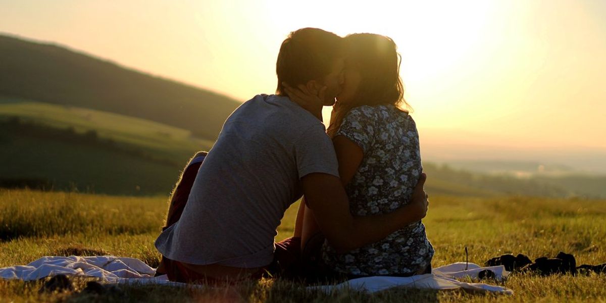 Szerelmespár naplementében csókolózik a földön ülve