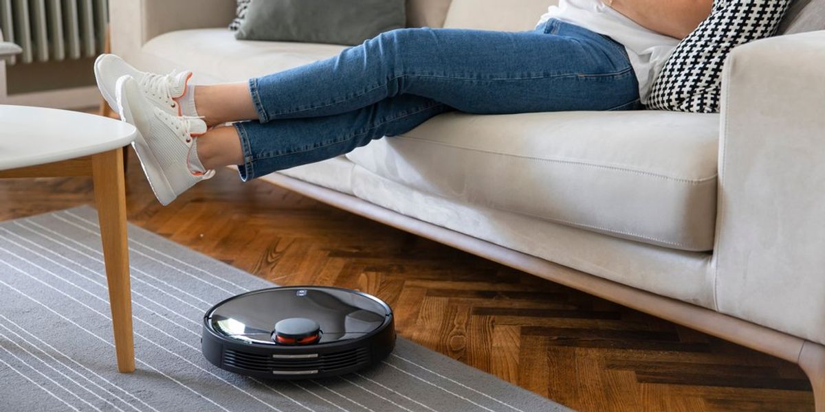 Robotporszívó, mellett kanapén ülő nő
