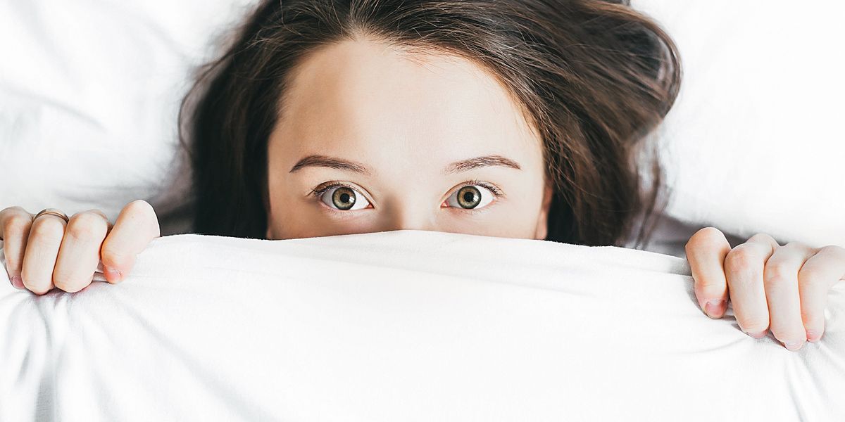 egy fiatal nő tágra nyitott szemekkel fekszik és magára húzza a takarót