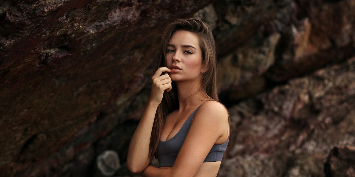 egy nő áll bikiniben a szikla előtt