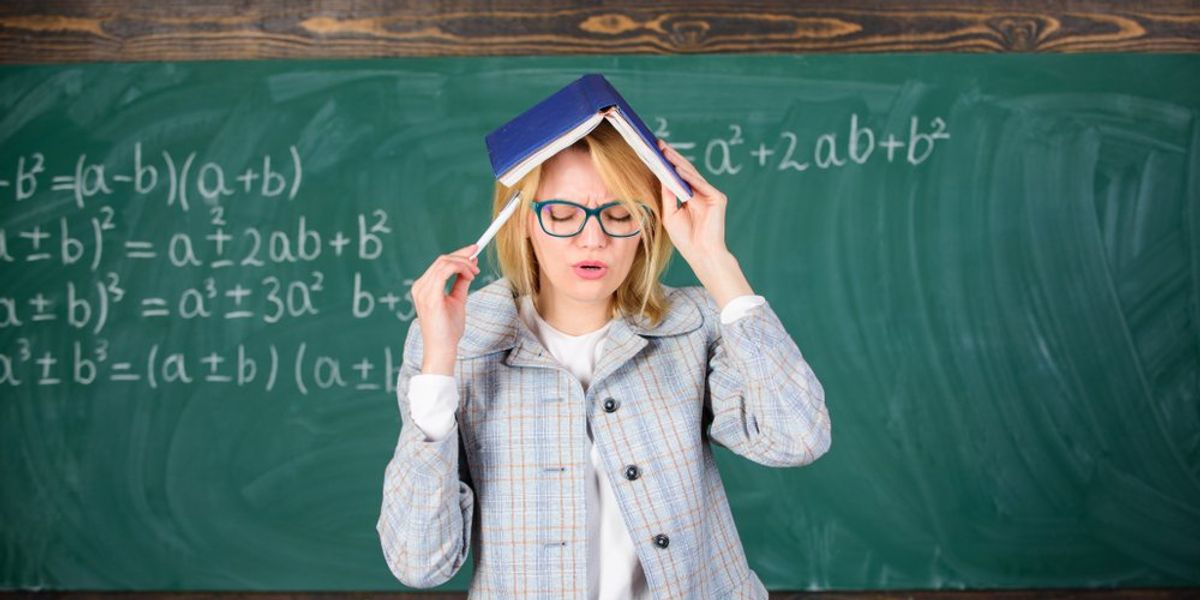 egy tanárnő a fejére mutat egy tollal, fején könyv, mögötte tábla, próbál felidézni valamit