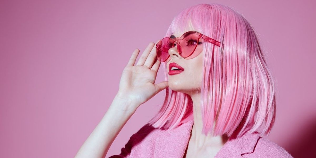 Rózsaszín hajú nő pink napszemüvegben néz a távolba