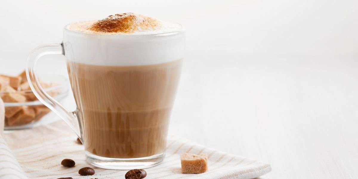 Latte világos konyhaasztalon, mellette kávészemek és barnacukor