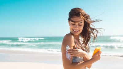 egy fiatal nő naptejet ken a tengerparton magára
