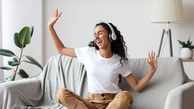 boldog nő táncol a kanapén ülve, fején fejhallgatóval