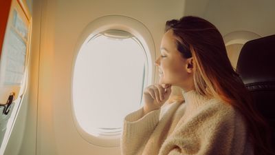 egy nő ül a repülőn mosolyogva az ablak mellett