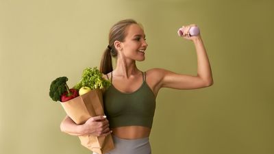 egy nő egyik kezében egy zacskó zöldség, másikban egy súlyzó