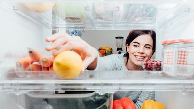 egy mosolygó nő a hűtőbe nyúl egy citromért