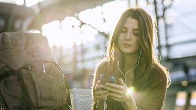 egy nő egyedül utazik és a telefonján épp zenét hallgat, mellette a hátizsákja
