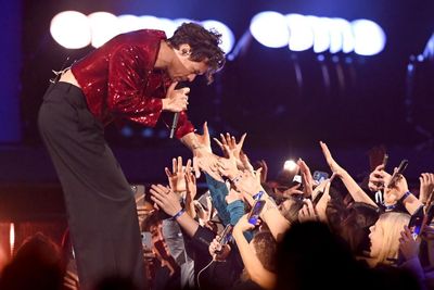 Harry Styles piros flitteres felsőben koncertet ad és a rajongói kezét fogja