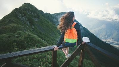egy hátizsákos nő ül hegyes környezetben és nézi a tájat egyedül