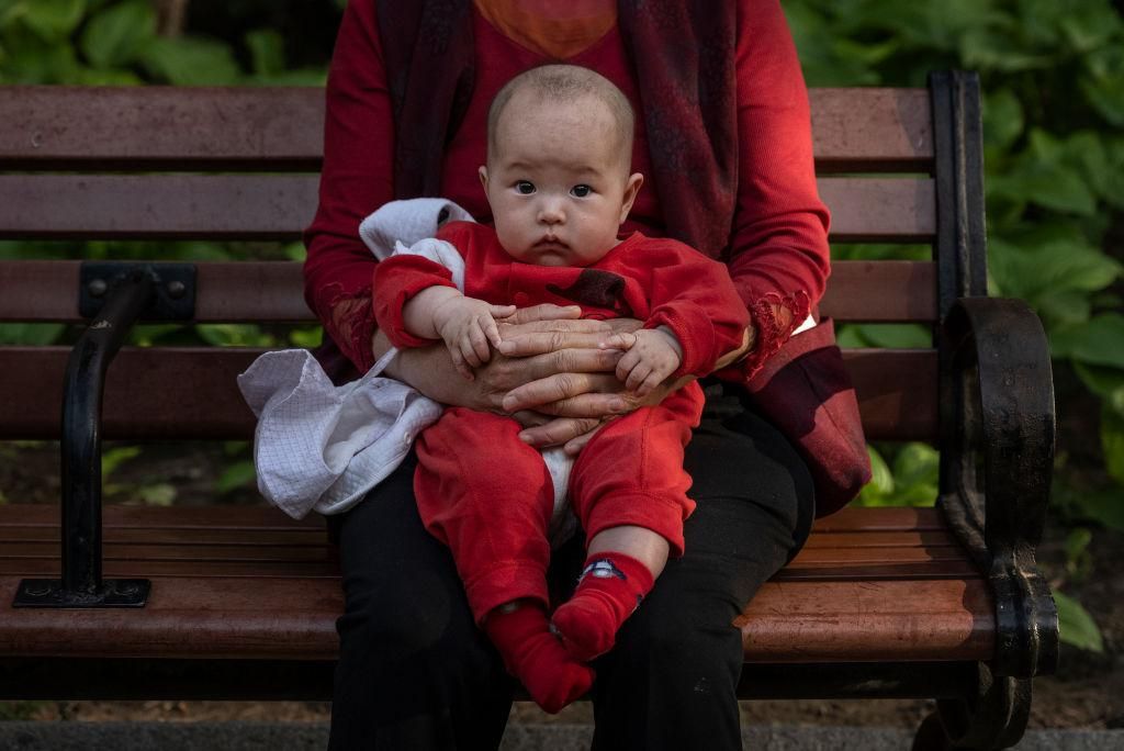 Egy nő karjában tartja gyermekét Pekingben