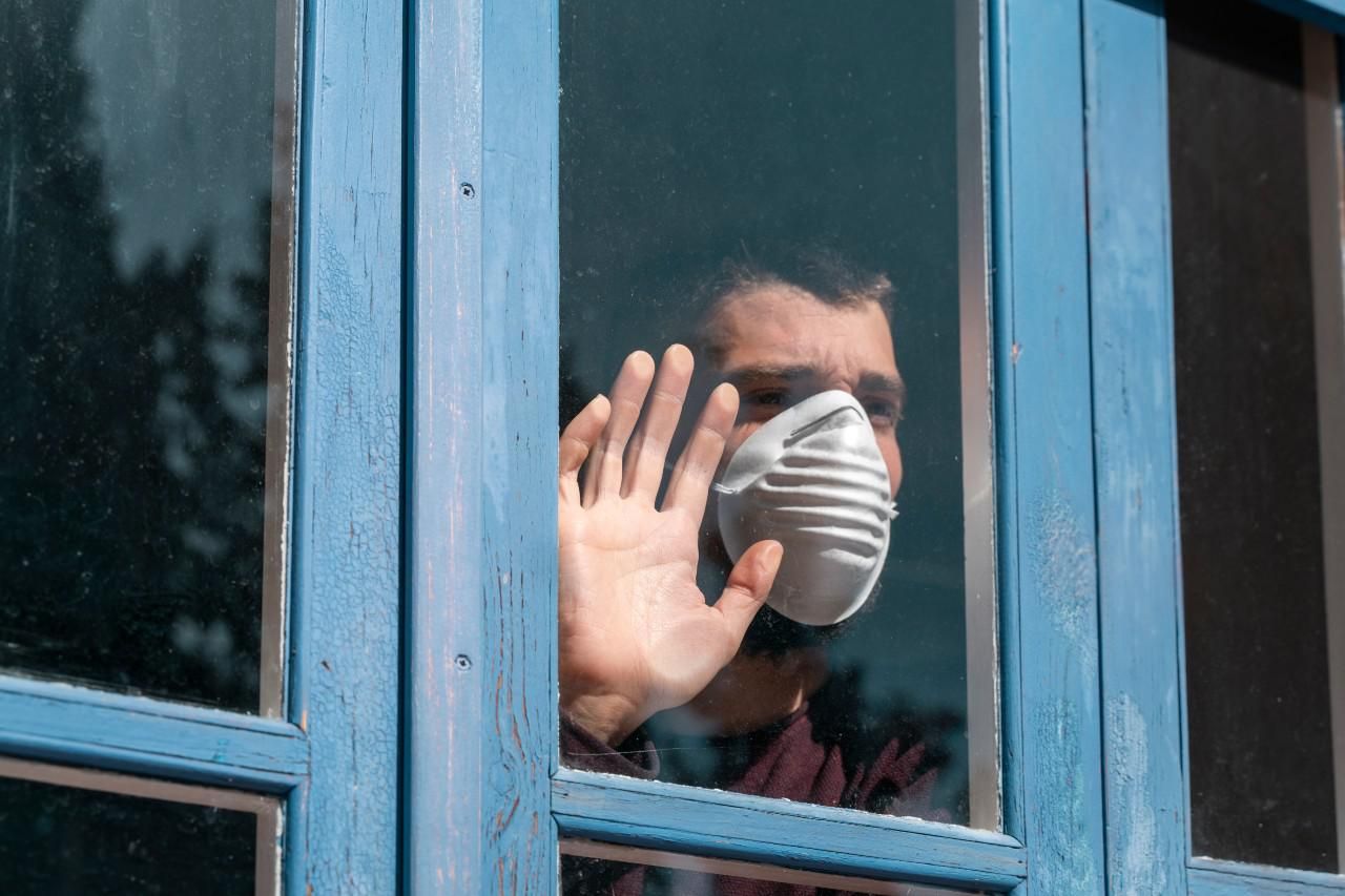 Maszkot viselő férfi a külvilágtól izoláltan áll az ablak előtt