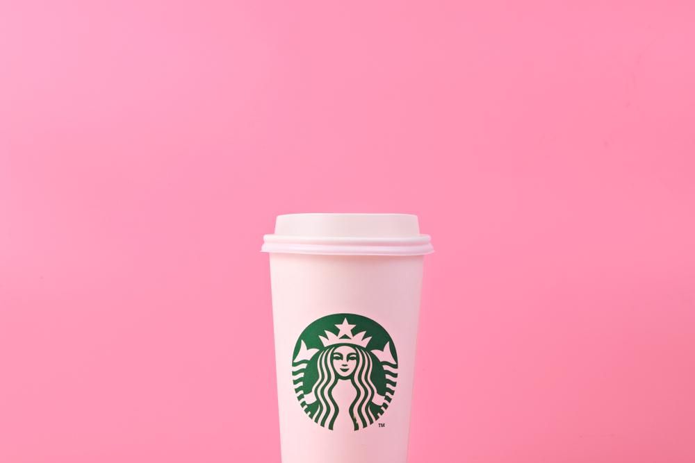 Starbucks logóval ellátott, egyszer használatos pohár rózsaszín háttér előtt