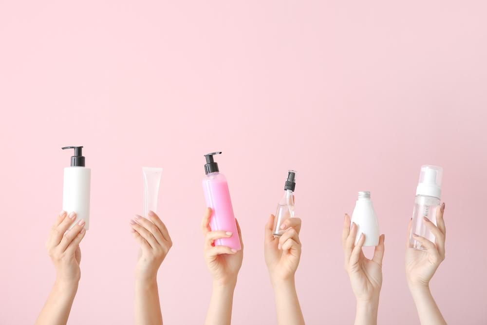 Különböző kozmetikai termékekeket tartó női kezek, rózsaszín háttér előtt