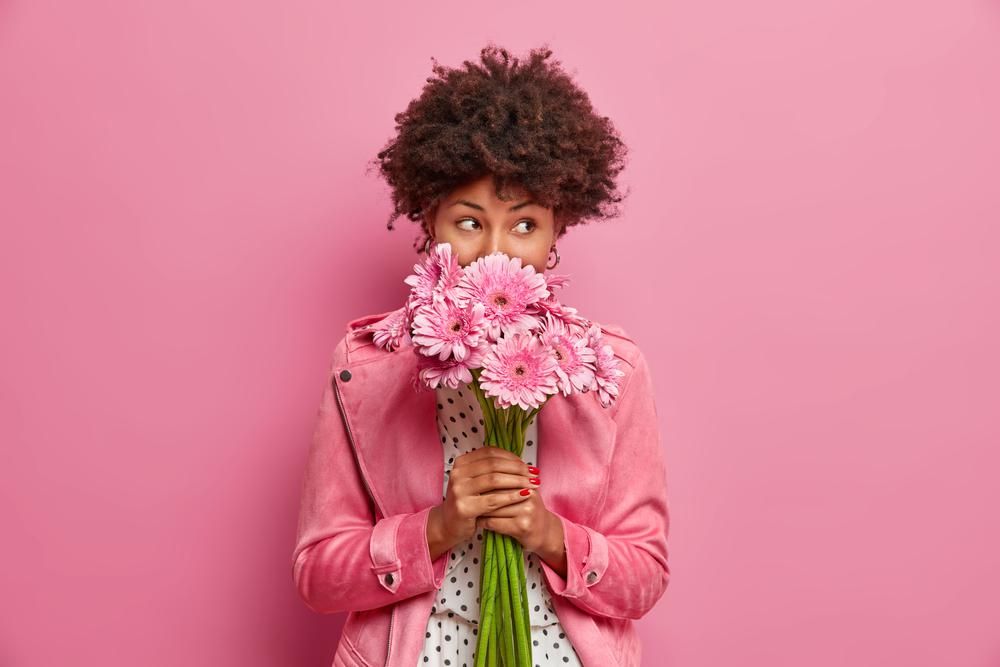 Fiatal nő a kezében tartott virágokat szagolja, rózsaszín háttér előtt