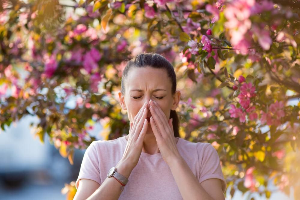 Fiatal nő virágzó fa  előtt tüsszent - tavaszi allergia 
