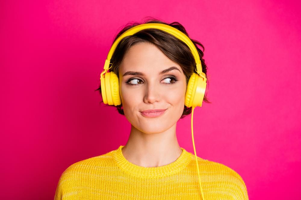 Fiatal nő podcastot hallgat rózsaszín háttér előtt